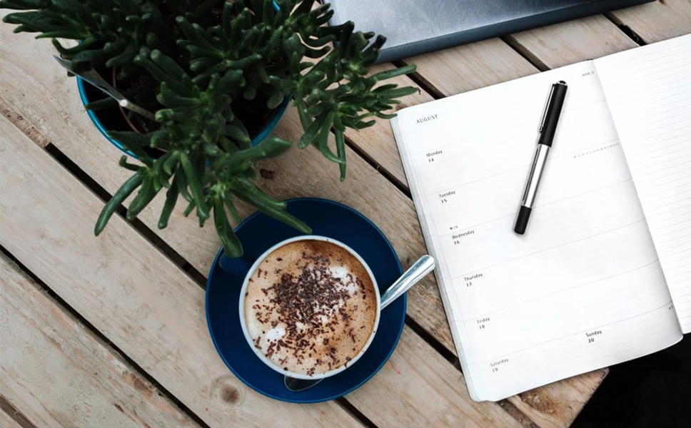 Web Designer in New York about page image_Coffee Cup, Planner Book, and Plan on a wooden table